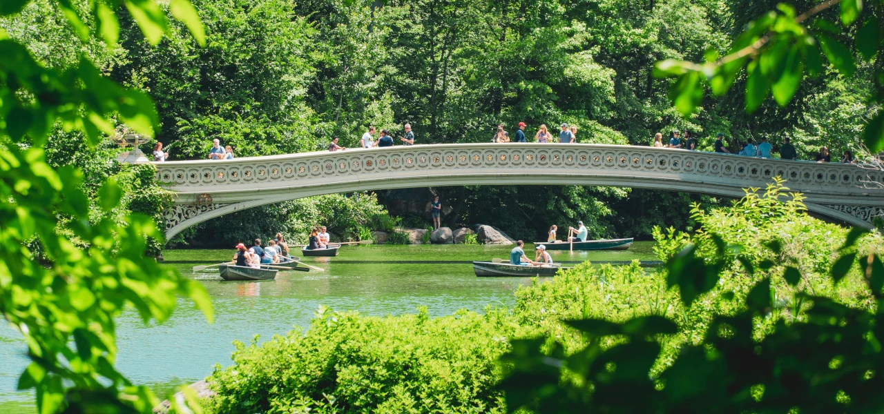 Menschen fahren in Paddelbooten unter einer Brücke im New Yorker Central Park