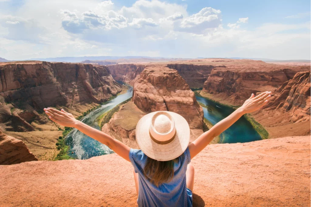 Eine Frau mit Hut steht mit ausgestrecketen Armen vor dem Grand Canyon