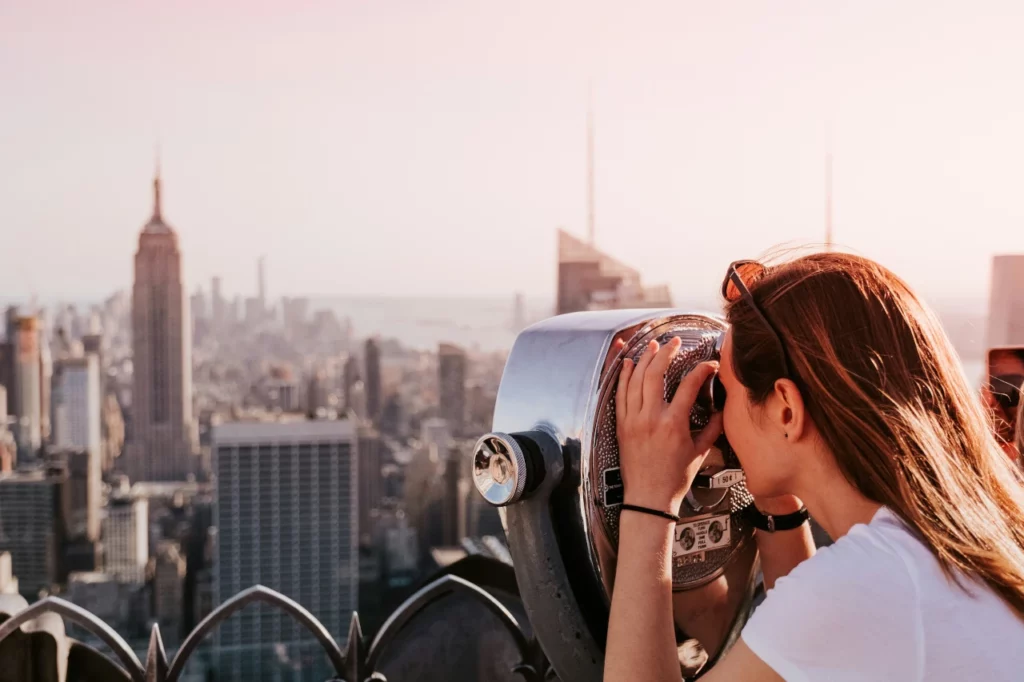 Eine Frau schaut durch ein Fernrohr auf die Skyline von Manhattan